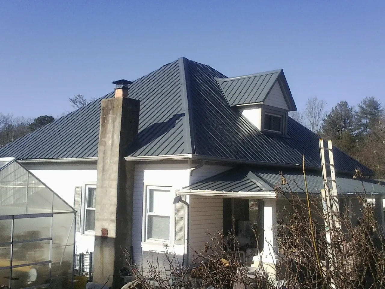Dark blue standing seam metal roof on a white farmhouse with dormer — Slate & Tile Roof Repair by Roofing Brothers in Dakota City
