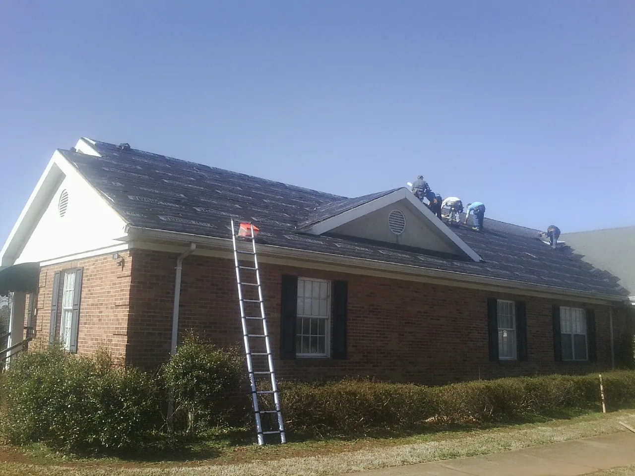 Crew tearing shingles off a brick ranch roof with a ladder set — Metal Roof Repair work by our crew in Dakota City