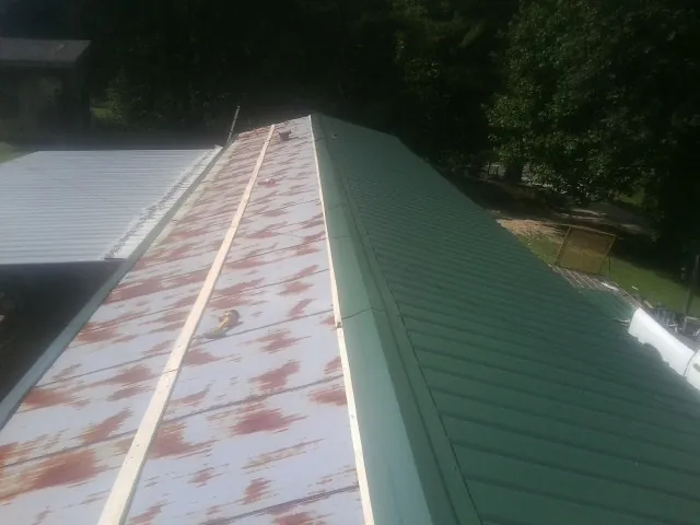 Old rusted panels beside newly installed green metal roofing — Wind Damage Roof Repair by Roofing Brothers in Dakota City