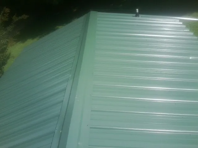 New green metal panels meeting at the ridge of a roof — Flat Roof Repair work by our crew in Dakota City
