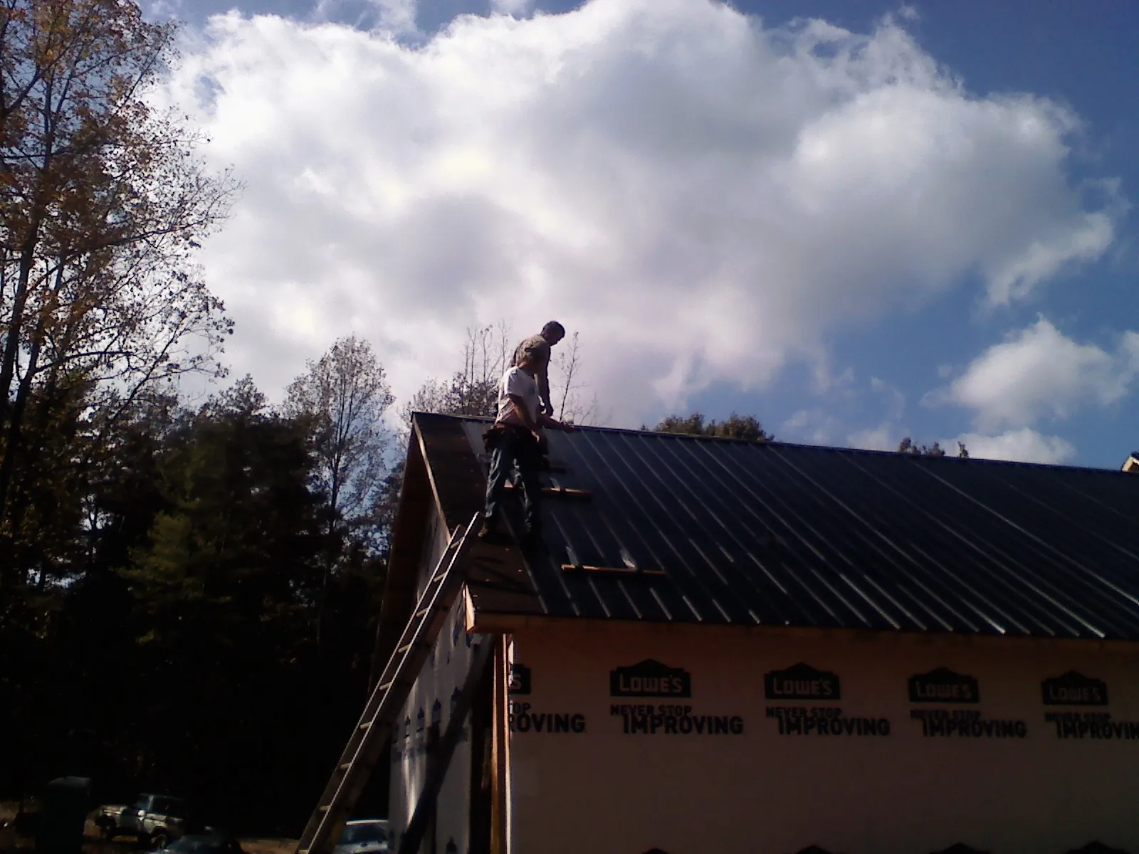 Roofer fastening dark metal panels high against a cloudy sky in Dakota City
