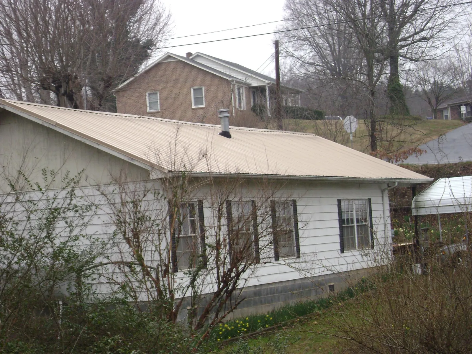 Tan metal roof on a white sided house set into a hillside — Commercial Roofing by Roofing Brothers in Dakota City